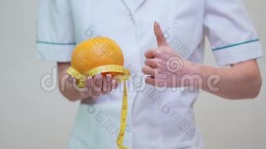 <strong>营养学家</strong>医生健康的生活方式理念-拿着橘子水果和量胶带